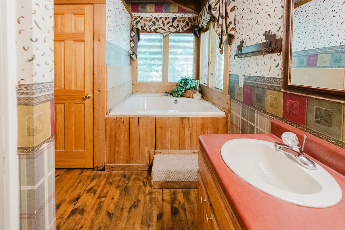 A tranquil master bathroom with a jacuzzi tub, rich wooden cabinetry, decorative wall patterns, and windows that fill the space with soft, natural light. The ambiance is spa-like and peaceful, perfect for rejuvenating baths.
