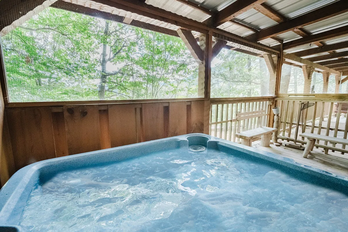 An interior view of a bubbling hot tub set against wooden railings, with green foliage visible outside. The hot tub is positioned to offer relaxing nature views, creating a tranquil space perfect for unwinding after group activities.