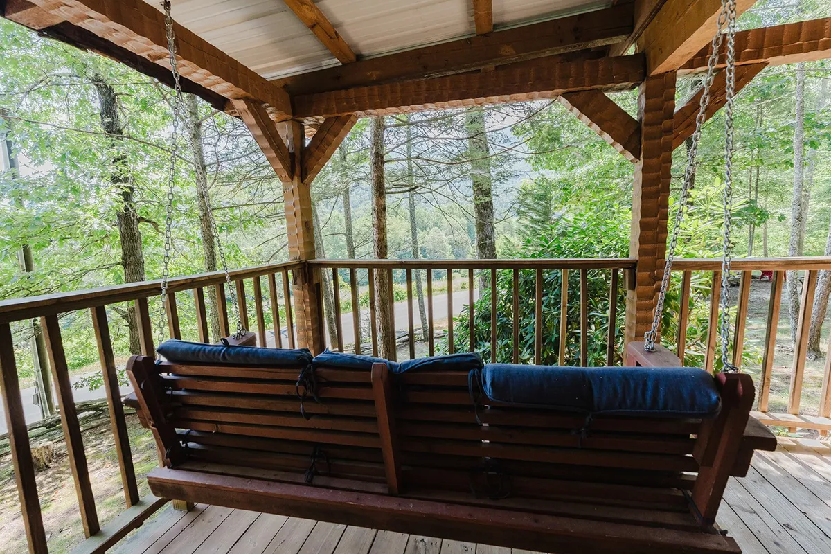 This image presents a swing seat nestled among tall trees with an expansive, open view. The composition evokes tranquility and immersion in nature, inviting guests to pause, listen to birdsong, and take in the valley sights and sounds referenced in the section content.