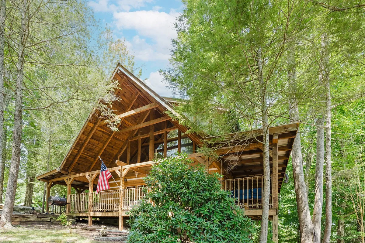 The image showcases the lodge's wooden exterior adorned with large windows, an American flag, and surrounded by tall trees. The porch is inviting, portraying a peaceful and welcoming retreat where families can relax after a day filled with local excursions.