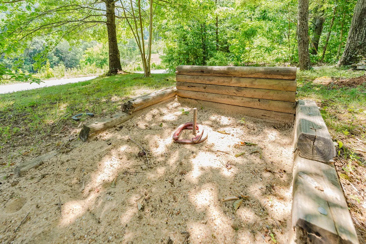 This joyful exterior scene features a sand pit, wooden seating, and a ring toss setup, with children engaged in outdoor play. The area exudes a playful, nostalgic feel and provides a clear visual of family-friendly activities available right outside the cabin, emphasizing the fun that awaits after using complimentary attraction tickets.